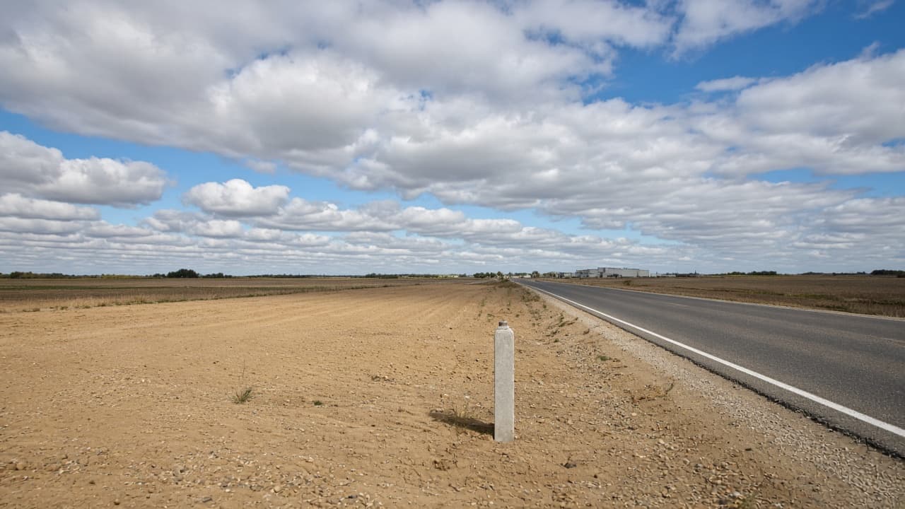 Graded commercial land at a road corner, with a concrete monument in the foreground.